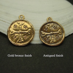 May include: Two round metal charms featuring a cross design with textured arms and small cross symbols in the quadrants. The left charm has a gold bronze finish, and the right charm has an antiqued finish. Each charm includes a small top loop.