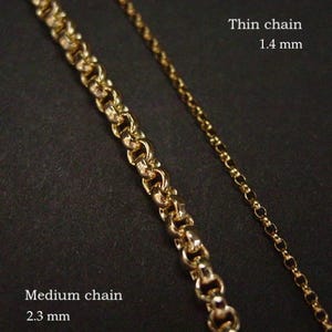 May include: Two gold-colored chains are displayed against a dark background. The text indicates one is a "Thin chain" at 1.4 mm, and the other is a "Medium chain" at 2.3 mm. The chains are likely for necklaces or bracelets.