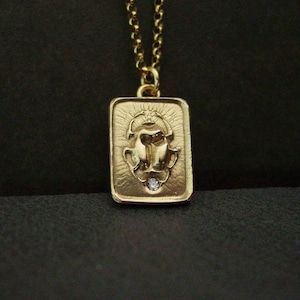 May include: Gold-toned rectangular pendant necklace featuring a detailed scarab beetle design. The pendant has a small diamond accent at the bottom. The necklace has a delicate gold chain.
