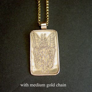 May include: A rectangular gold-toned pendant featuring an engraved illustration of a figure with large butterfly wings. The pendant is suspended from a medium-weight gold-toned chain. The text "with medium gold chain" is visible at the bottom.