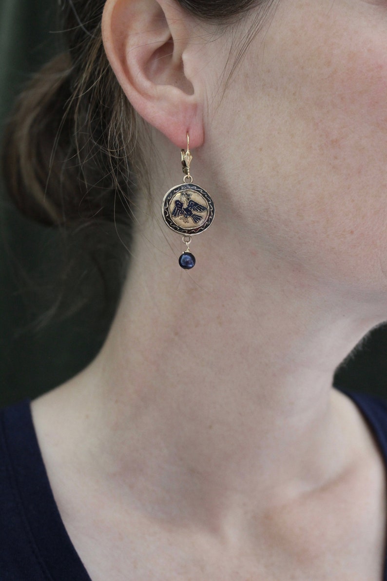 May include: Gold tone earrings with a black enamel eagle design and a dangling black bead.