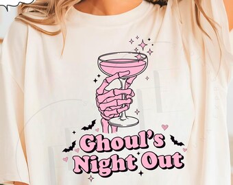 Puede incluir: Camiseta color crema con un gráfico rosa. El gráfico presenta una mano esquelética sosteniendo un cóctel rosa, con las palabras "Ghoul's Night Out" en rosa y negro. Murciélagos y estrellas completan el diseño.