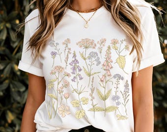 May include: White t-shirt with a floral print featuring various types of flowers in shades of pink, purple, and blue.