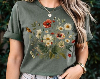 May include: A green short-sleeved t-shirt with a floral print featuring red poppies, white daisies, and a butterfly. The print also includes a dragonfly and a ladybug.