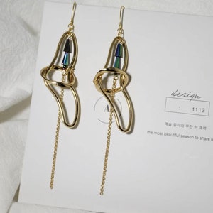 May include: A pair of gold-toned earrings with a dangling chain. The earrings feature a geometric design with a small cluster of iridescent green and blue stones.