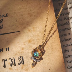 Overhead shot of the Felix Felicis lucky potion necklace with an iridescent opal, resting on a vintage book page to create a magical, bookish vibe.