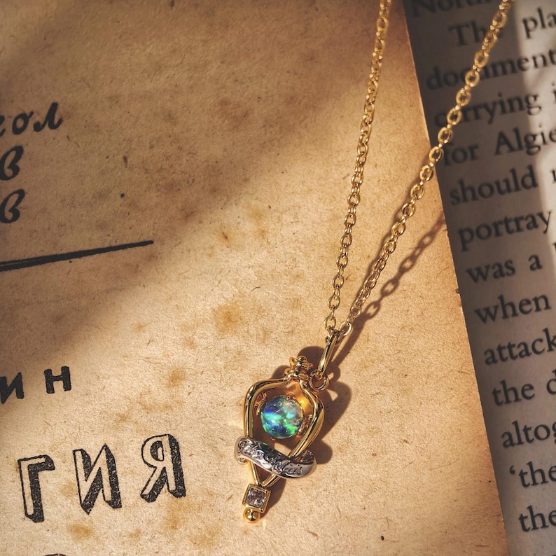 Overhead shot of the Felix Felicis lucky potion necklace with an iridescent opal, resting on a vintage book page to create a magical, bookish vibe.