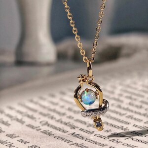 Detailed close up of the Felix Felicis potion bottle pendant, highlighting the quality of the opal and gold finish on a vintage paper background.