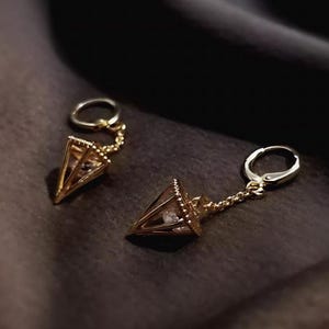 May include: A pair of gold-tone earrings with a geometric diamond shape design. Each earring features a small clear crystal in the center of the diamond shape.