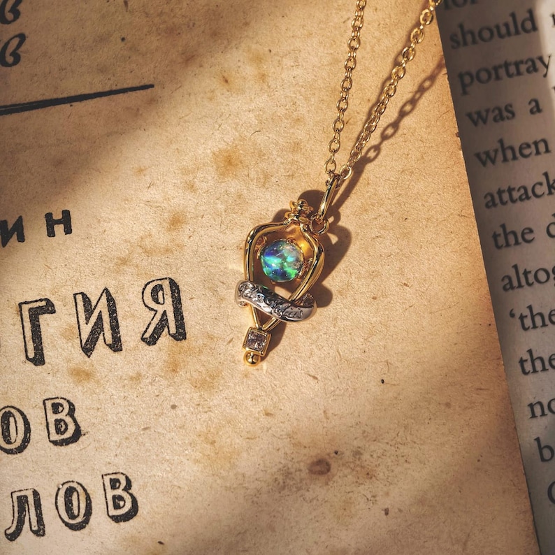 Overhead shot of the Felix Felicis lucky potion necklace with an iridescent opal, resting on a vintage book page to create a magical, bookish vibe.