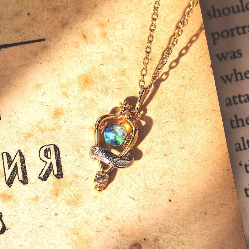 Overhead shot of the Felix Felicis lucky potion necklace with an iridescent opal, resting on a vintage book page to create a magical, bookish vibe.