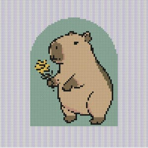 Op de afbeelding: Een kruissteekpatroon met een gepixelde beige capibara met een donkerbruin gezicht en poten, die een kleine gele bloem vasthoudt. De capibara is gecentreerd in een lichtgroene boogvorm tegen een lichtpaarse en witte gestreepte achtergrond.