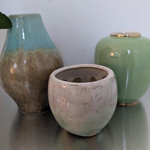 May include: Three ceramic vases in different sizes and colors. The largest vase is a light blue and brown color, the medium vase is a light green color, and the smallest vase is a white and light green color.