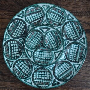 Può includere: Un piatto da portata rotondo in ceramica con 12 scomparti individuali, ognuno decorato con un motivo a scacchi verde e bianco. Il piatto ha un bordo rialzato e un bordo smerlato.