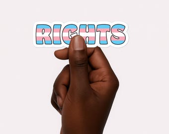 May include: A sticker with the word "RIGHTS" in bubble letters. The letters are colored in the transgender pride flag colors: light blue, pink, and white. The sticker is held between two fingers against a white background.