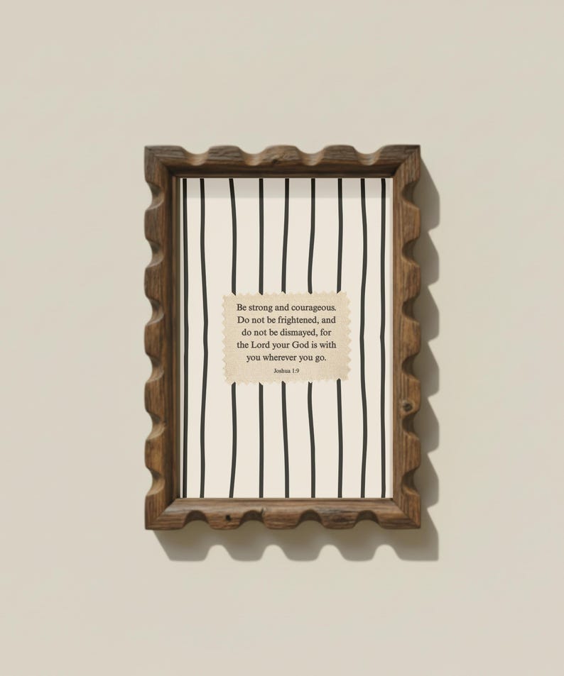 May include: A framed print with a wood-tone scalloped edge. The print features a white background with black vertical lines. A tan-colored rectangle with text is centered on the print, which reads "Be strong and courageous...Joshua 1:9."