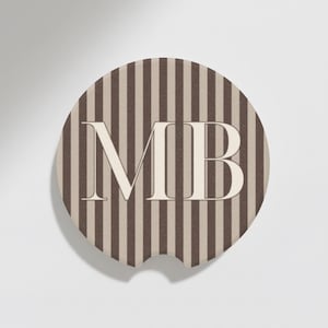 May include: Circular car coaster with a brown and beige striped design. The coaster displays the letters "MB" in a serif font. It has a small notch for easy removal from a car cup holder.