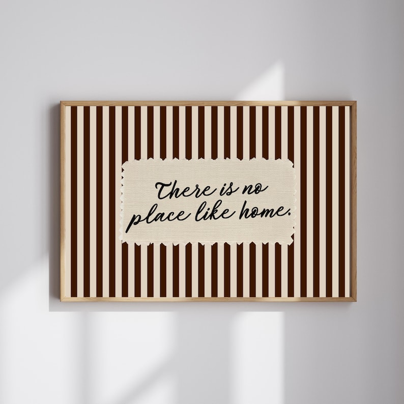 May include: A framed print with a brown and cream striped pattern. The artwork displays the phrase "There is no place like home" in black script on a textured, cream-coloured rectangle.