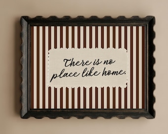 May include: A framed wall art piece with a decorative border. The artwork features a background of brown and cream vertical stripes. A cream-colored rectangle in the center displays the text "There is no place like home."
