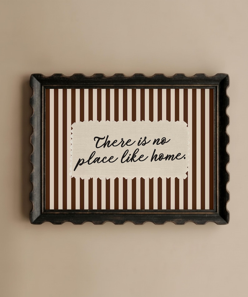 May include: Framed wall art with a decorative border. The artwork has a background of brown and cream vertical stripes. A cream rectangle in the centre displays the text "There is no place like home."