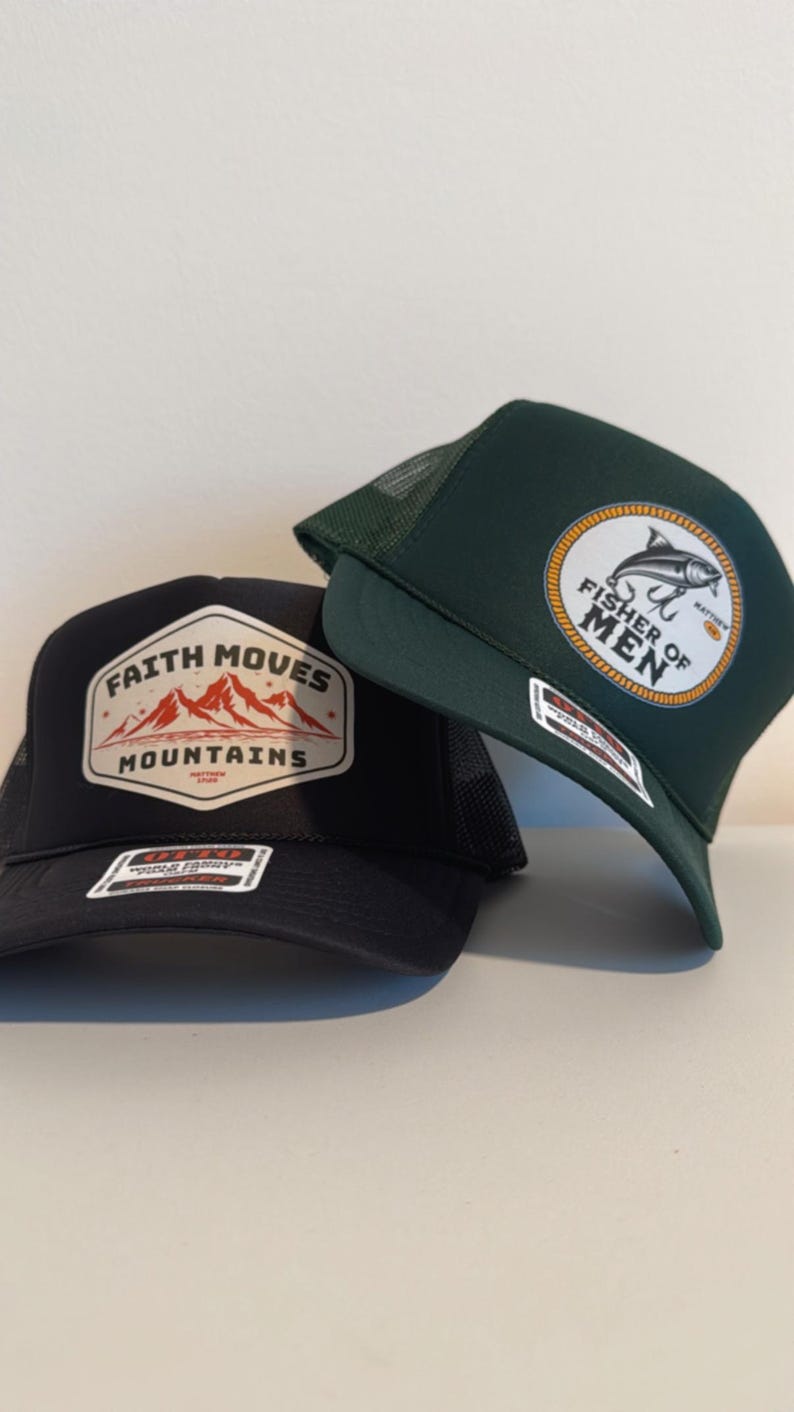 Puede incluir: Dos gorras de camionero. Una gorra negra con un parche con el texto "Faith Moves Mountains" y un gr&aacute;fico de monta&ntilde;a. La otra es verde oscuro con un parche que dice "Fisher of Men" y un gr&aacute;fico de pez.