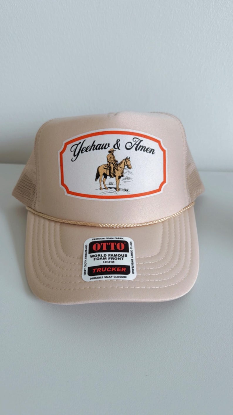 Puede incluir: Gorra trucker color beige con un gr&aacute;fico "Yeehaw & Amen" que muestra a un vaquero a caballo. La gorra tiene una parte trasera de malla y un detalle de cuerda en el borde. Tiene un cierre a presi&oacute;n duradero y una etiqueta OSFM.