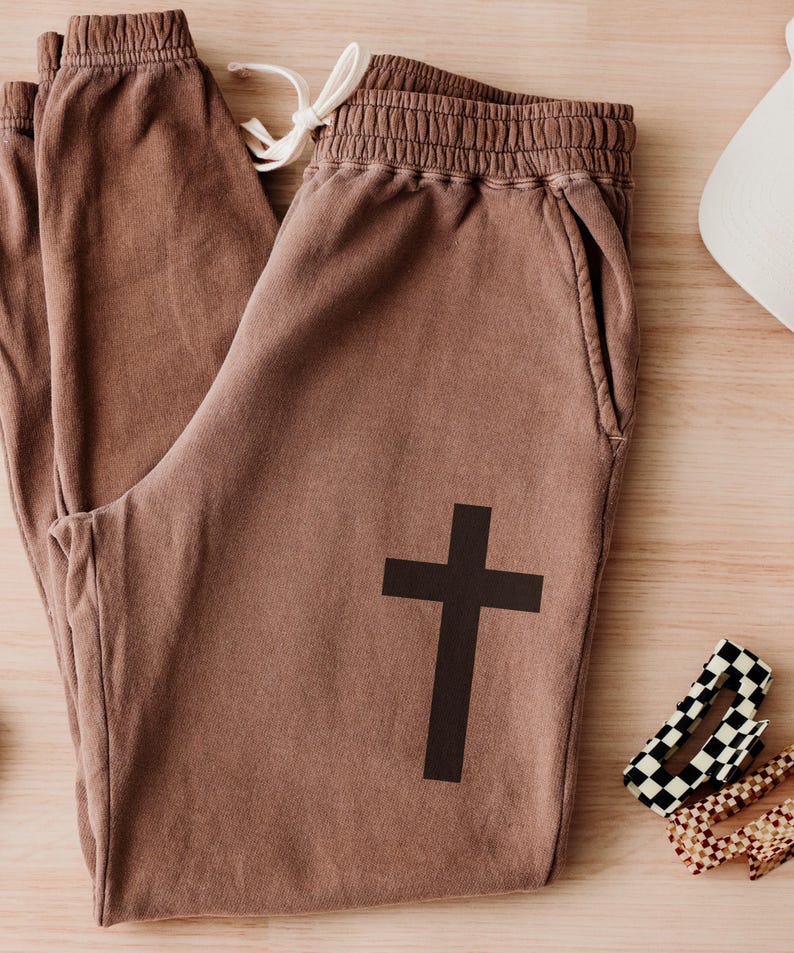 May include: Brown sweatpants with a black cross graphic on the left leg.