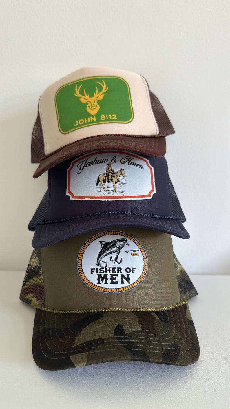 Puede incluir: Una pila de cuatro gorras de camionero con diferentes dise&ntilde;os. La gorra superior es beige y marr&oacute;n con un rect&aacute;ngulo verde y el texto "JOHN 8:12". La segunda gorra es azul marino con un gr&aacute;fico de vaquero y caballo. La tercera tiene un gr&aacute;fico de pez y el texto "FISHER OF MEN". La gorra inferior es de camuflaje.