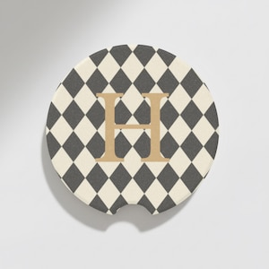 May include: A round car coaster with a black and cream diamond pattern and a gold letter "H" in the center. The coaster has a small notch for easy removal from a car cup holder. This item is a decorative car accessory.