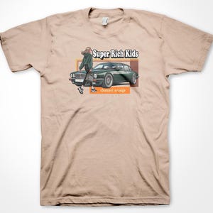 May include: A beige t-shirt with a graphic print of a woman walking past a green Jaguar car. The text "Super Rich Kids" and "channel orange" are printed on the shirt.