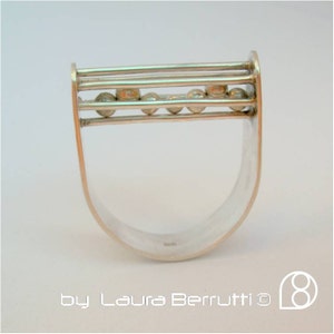 Könnte beinhalten: Ein silberner Ring mit geometrischem Design und kleinen runden Perlen. Der Ring ist oben und unten offen, und die Perlen sind in einer Reihe über der Oberseite angeordnet.