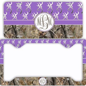 May include: A license plate and license plate frame set featuring a purple and camouflage design. The top portion has a purple background with a pattern of silver deer silhouettes. The center has a monogram. The bottom has a camouflage pattern.