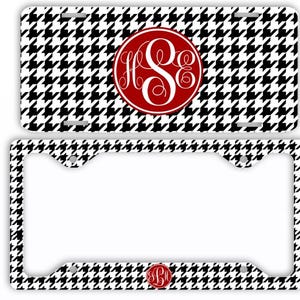 May include: A license plate and frame set featuring a black and white houndstooth pattern. The license plate has a red circle with a white monogram. The frame has a matching houndstooth pattern and a small red monogram at the bottom.