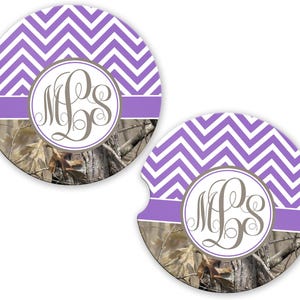 May include: Two round car coasters with a purple and white chevron pattern. Each coaster features a monogram in a circle, with a purple band and a camouflage background.