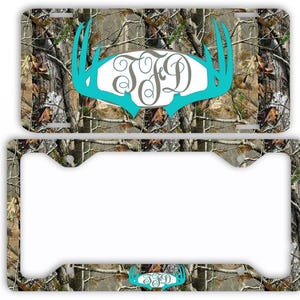 May include: A license plate and frame set with a camouflage pattern. The license plate features a teal antler design with a monogram. The frame has a matching camouflage pattern and a smaller teal antler design.