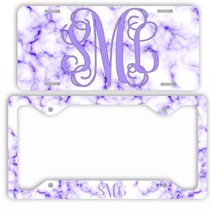 May include: A license plate and frame set featuring a purple marble design. The license plate has a large, stylized letter "M" in a lighter shade of purple. The frame has a matching marble pattern and a smaller "SM" monogram.