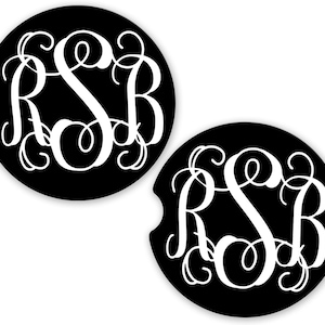 May include: Two black car coasters with a white monogram design featuring the letters "RSB" in a decorative, swirling font. The coasters have a circular shape with a small notch on one side.