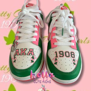 May include: Pair of white, green, and pink Nike sneakers with white laces. The sneakers feature the text "AKA" and "1908" in pink and green. The shoes have a green sole and pink accents.