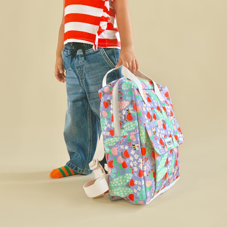 Child holding a floral kids backpack with white straps - lightweight and easy to carry, perfect for everyday adventures.