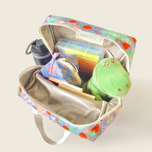 Open kids backpack with floral print showing spacious interior, water bottle, toy dinosaur, and pencil case - perfect for school or travel essentials.