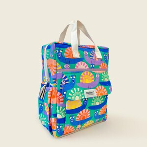 Colorful kids backpack with cheerful snail print on a bright blue background, featuring a front pocket, side pouch, and white handles - fun and durable for everyday use.