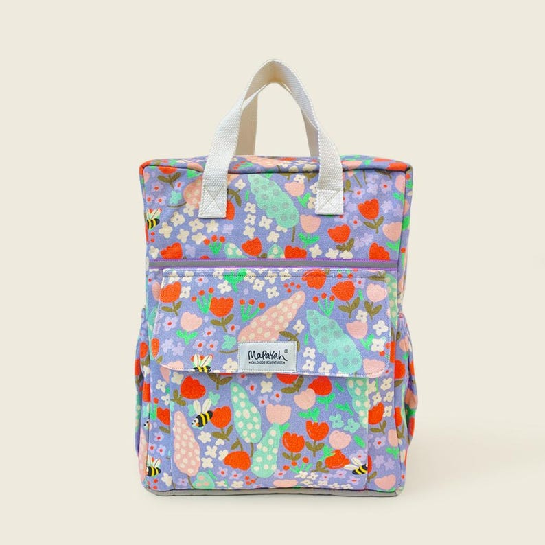 Kids backpack with colorful floral and bee print, featuring a front pocket, side pouch, and white handles - cute and sturdy bag for school or outings.