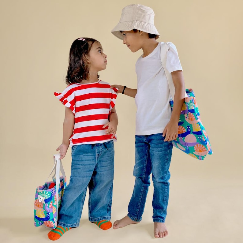 Two young children carrying matching printed canvas tote bags from Mapayah’s kids collection.
