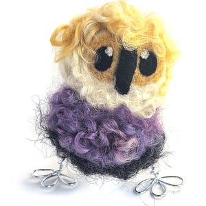May include: A small, felted owl made with yellow, white and purple wool. The owl has black eyes and a black beak. The owl is standing on two wire legs.