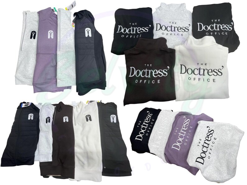 May include: A collection of various sweatshirts and hoodies in different colors, including gray, black, white, and purple. Some of the sweatshirts have the text "The Doctress' Office" printed on them.