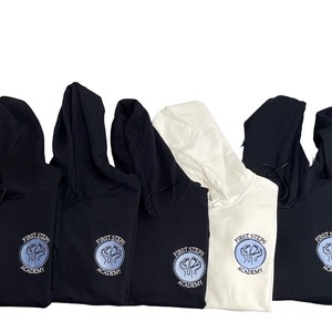 May include: Six black and white hooded sweatshirts with the logo "First Steps Academy" embroidered on the front. The logo is a circle with a blue and white design inside.