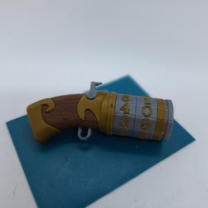 May include: A gold and brown toy pistol with a silver barrel and a rotating cylinder with numbers 1, 0, 9, 6, 5, 4, 3, 2, and 8.
