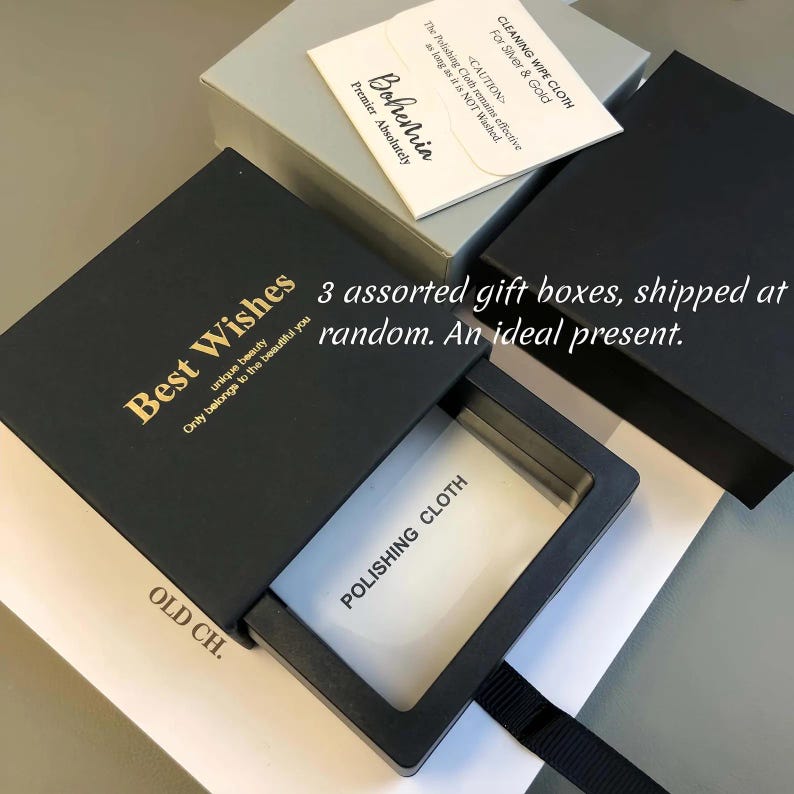 May include: Three square black gift boxes with gold text reading Best Wishes, unique beauty, Only belongs to the beautiful you. One box is partially open, revealing a white card labeled POLISHING CLOTH. A white cleaning cloth card is also included.