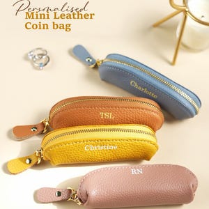May include: Several small, oval-shaped leather coin purses in shades of blue, brown, yellow, and pink. Each purse has a gold zip and a name or initials printed on it. The text "Personalised Mini Leather Coin bag" is visible.