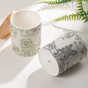 May include: Two white ceramic plant pots with floral and pet illustrations. One pot features a Pomeranian with the name "Tucker" and the years "2010-2024". The other pot displays a French Bulldog with the name "Milo".
